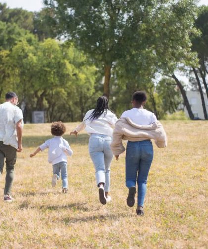 Cheerful family walking together in a sunny park surrounded by trees.