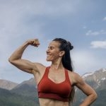 Woman in red sportswear flexing muscles against a scenic mountain backdrop.