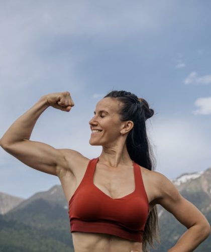 Woman in red sportswear flexing muscles against a scenic mountain backdrop.
