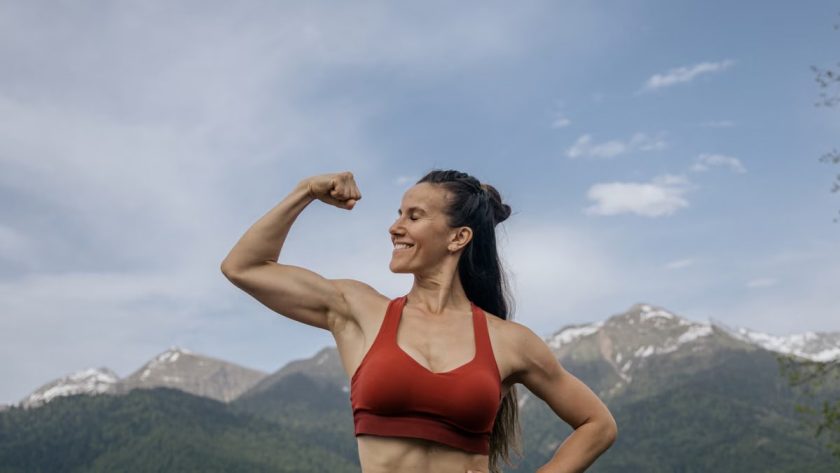 Woman in red sportswear flexing muscles against a scenic mountain backdrop.